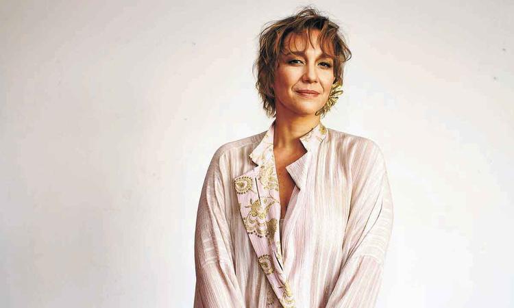 De camisa branca com detalhes dourados, Raquel Coutinho sorri para a cmera
