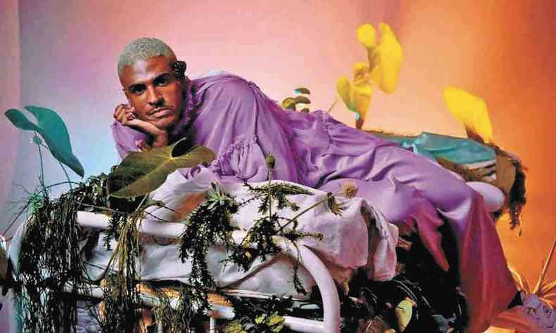 Vestido com tnica violeta, Rico Dalasam posa para foto deitado em poltrona 