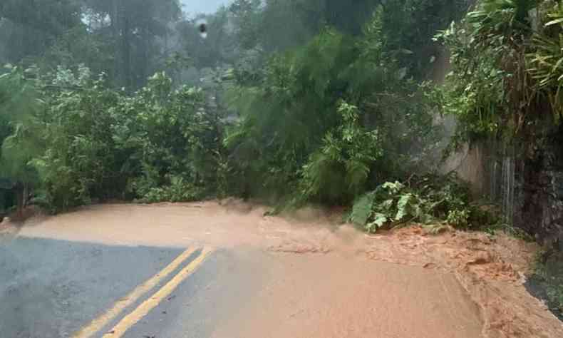 Imagem mostra rodovia interditada com rvores derrubadas. Parte da rodovia tambm est interditada com chuva e lama