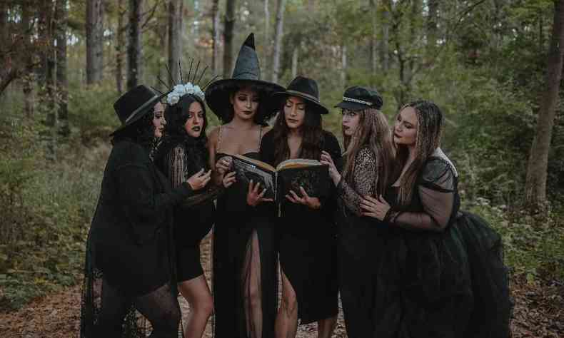 Grupo de seis mulheres, vestidas como bruxas em trono de um livro, em uma floresta