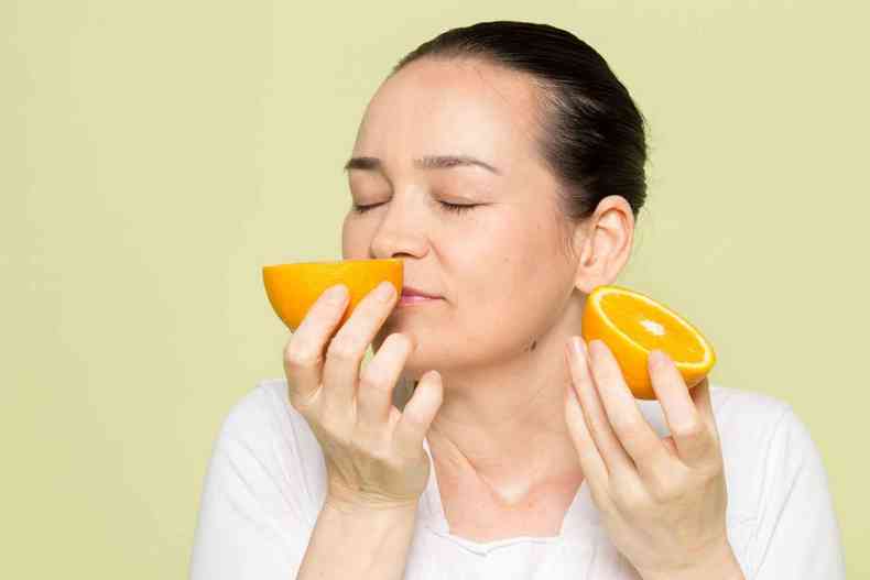 Mulher cheirando a metade de uma laranja