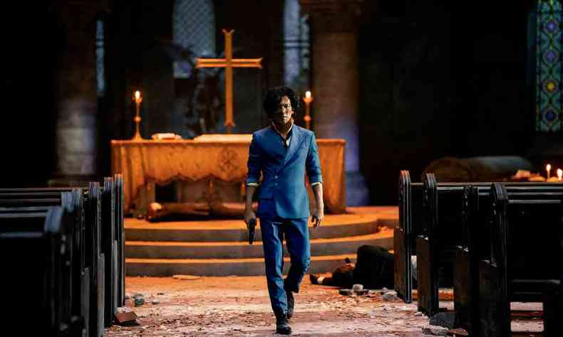 Dentro de uma igreja, o ator John Cho caminha com a arma na mo, o altar ao fundo e um corpo entre os bancos, durante cena da srie ''Cowboy Bebop'' 