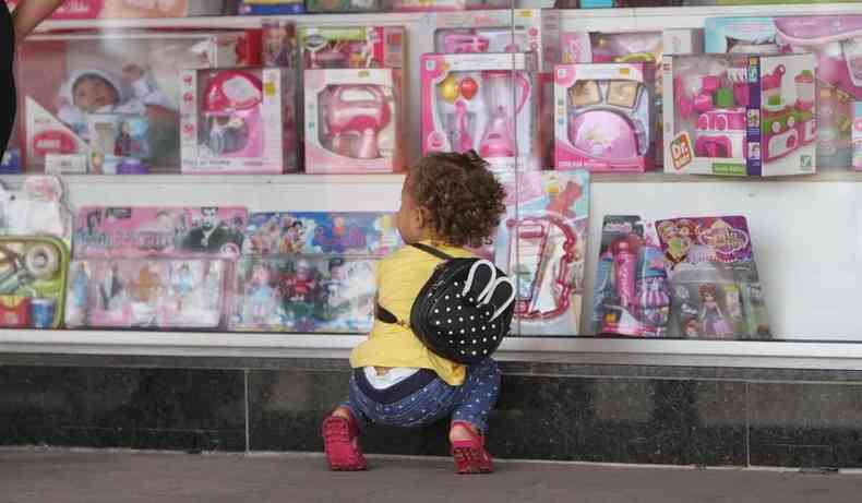 Criana olhando em vidro de loja com brinquedos.