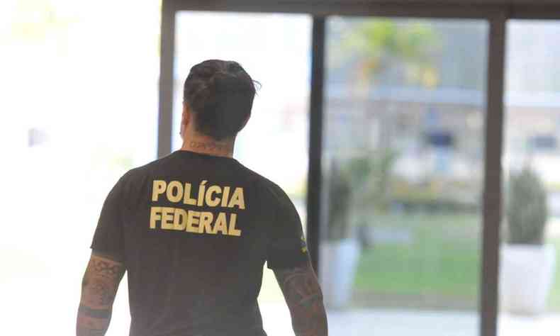 Foto meramente ilustrativa mostra agente de costas com uma camisa preta com a inscrio 'Polcia Federal'. Ao fundo, a imagem est embaada e aparece uma porta de vidro