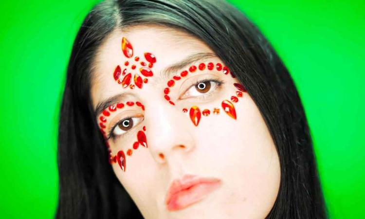 Usando contas vermelhas na testa e ao redor dos olhos, a artista Sara No Tem Nome olha para a cmera