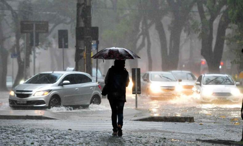 Pessoa na chuva com um guarda-chuva preto e carros passando na rua