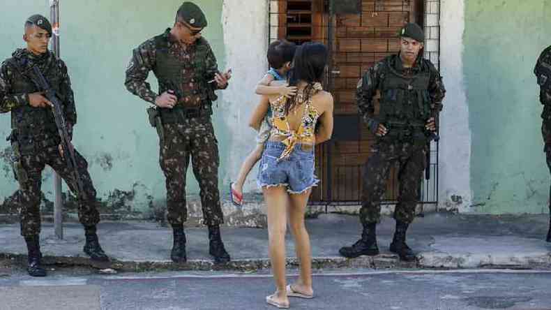 Militares fardados e armados em frente a casa e mulher com criana de costas