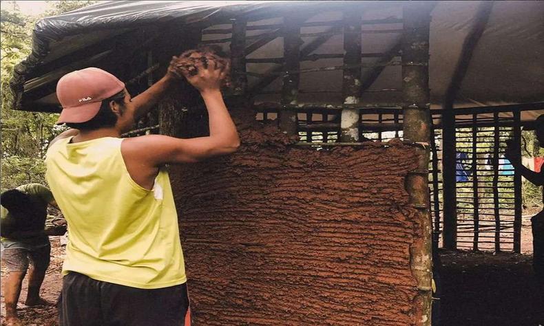 Homem colocando barro em parede de oca