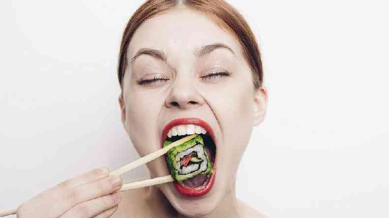 Mulher abrindo a boca para comer sushi, de olhos fechados