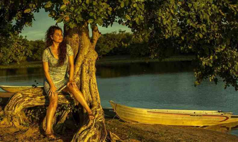 Atriz Isabel Teixeira na beira do rio, ao lado de canoa, na novela Pantanal