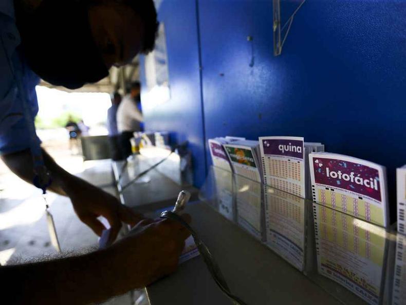 Na imagem h uma pessoa marcando suas apostas em um bilhete de loteria em uma mesa 