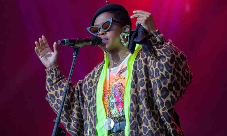 Usando culos escuros com aros em formato de corao, Lauryn Hill canta, com os braos abertos,em frente ao microfone