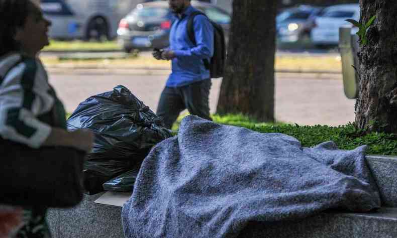 Pessoa coberta deitada na rua ao lado de saco de lixo