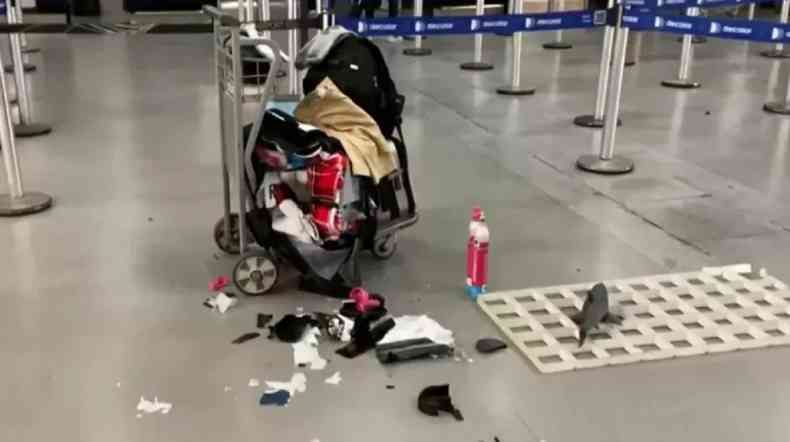 carrinho de aeroporto com bagagens danificadas e pedaos de malas espalhados no cho