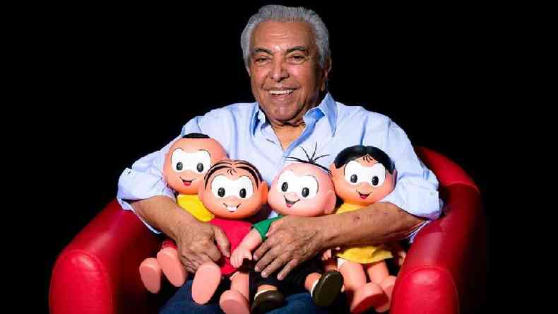 Mauricio de Sousa sentado em sof segurando bonecos de personagens da turma da Mnica