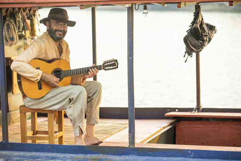 Almir Sater sorri e toca viola dentro de chalana em cena da novela Pantanal