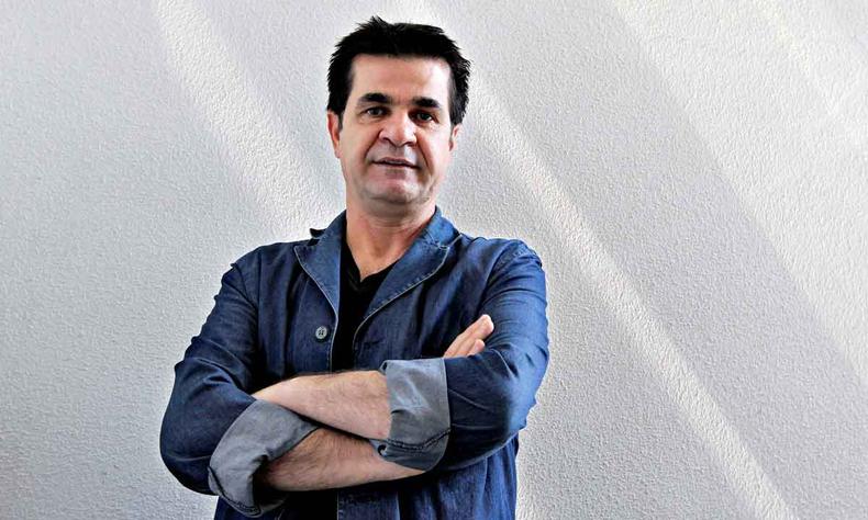 De camisa jeans, Jafar Panahi cruza os braos, com parede cinza ao fundo 
