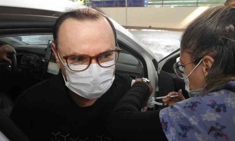Enfermeira aplica vacina contra a COVID no braço de um homem sentado no banco de um carro