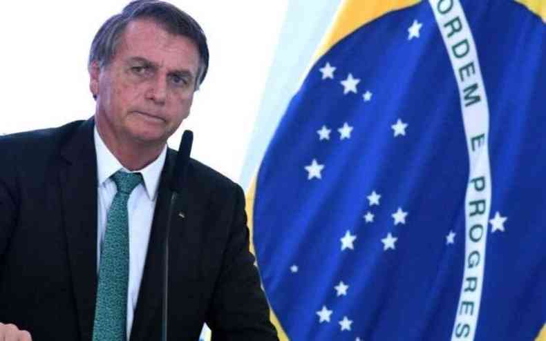 Bolsonaro senta ao lado da bandeira do Brasil