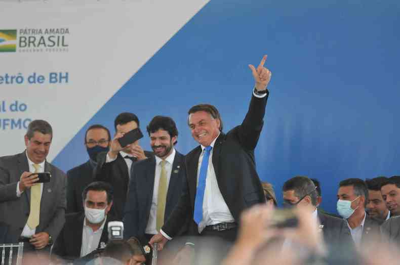 Presidente Jair Bolsonaro sentado, faz sinal de arma com a mo
