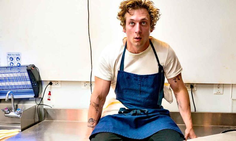 Ator Jeremy Allen White est sentado em bancada de cozinha em cena da srie O urso