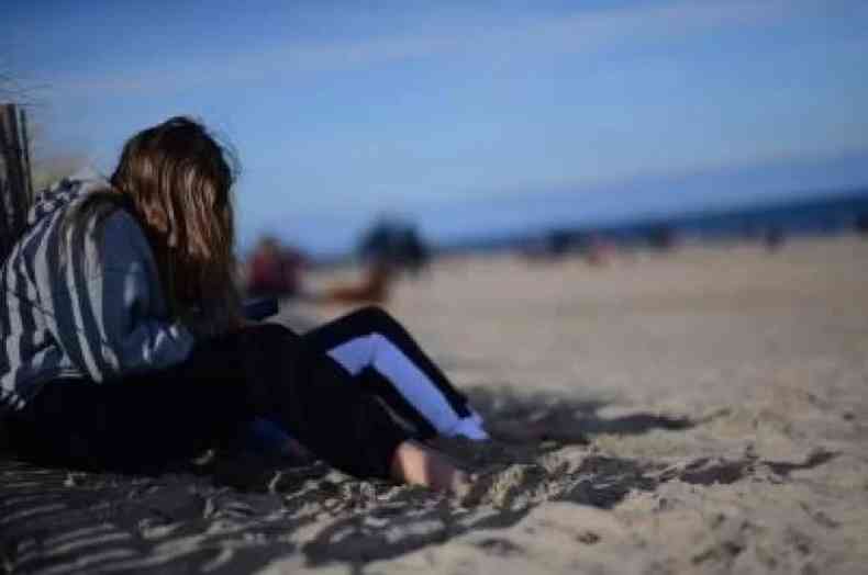 Menina olhando celular sentada na praia