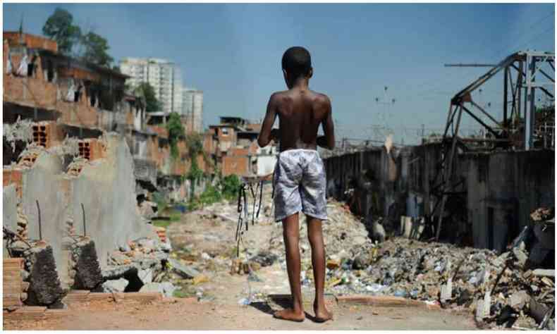 Menino de costas, segurando uma pipa, em frente a um cenrio de pobreza e destruio 