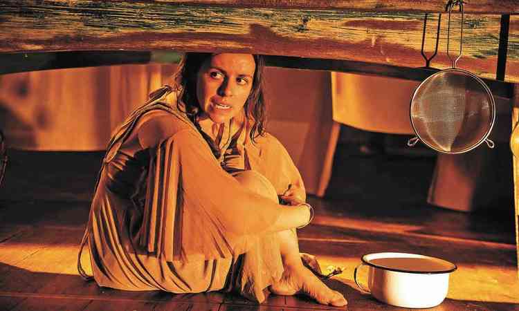A atriz Raquel Penner sentada debaixo de mesa em cena do monlogo 'Cora do Rio Vermelho'