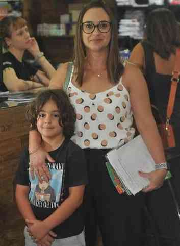 Karina usando uma roupa branca ao lado do filho Theo, com uma roupa preta e azul