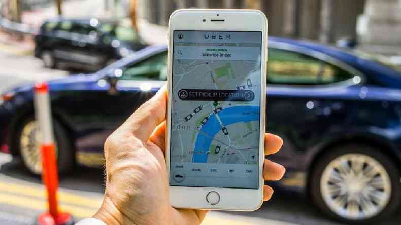 Mo segura celular com o aplicativo Uber na tela, visto de dentro de um carro