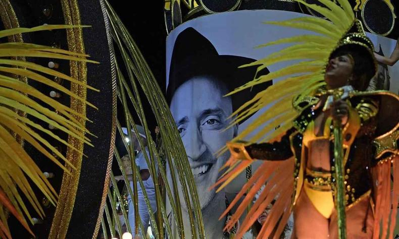 Destaque samba em carro que homenageia ator Paulo Gustavo; ao fundo, o rosto dele