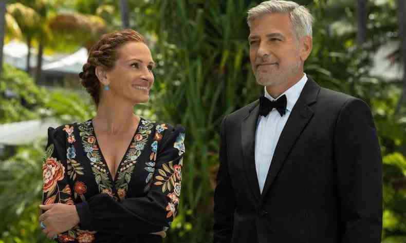 Julia Roberts, de braos cruzados e cabelos presos, sorri e olha para George Clooney, de smoking, em cena do filme Ingresso para o paraso