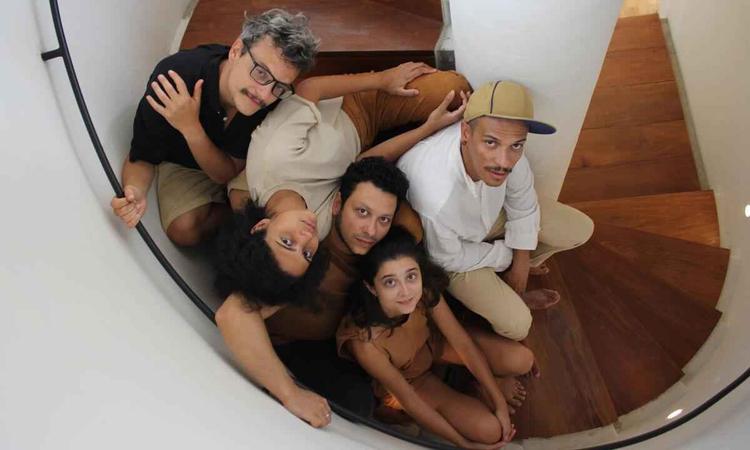 Integrantes da banda Graveola esto sentados em escadaria em forma de caracol e olham para o alto
