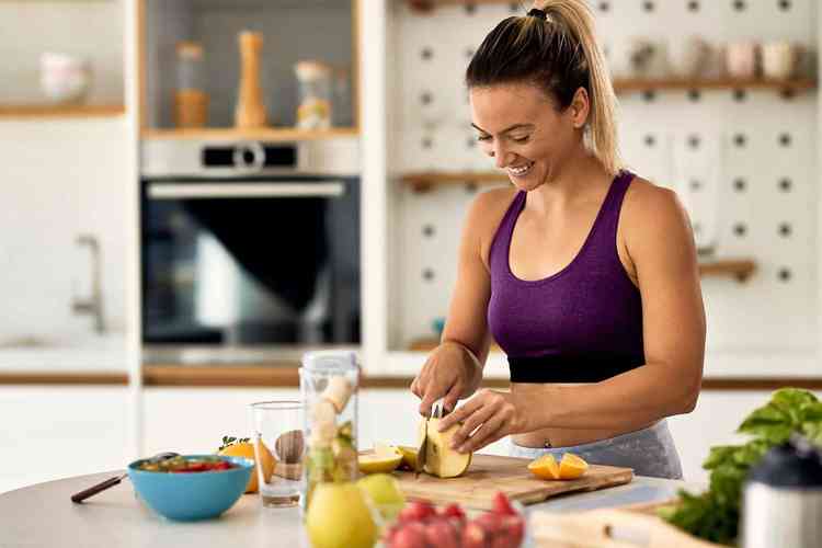 Mulher com roupa de exercício preparando sua refeição saudável na cozinha