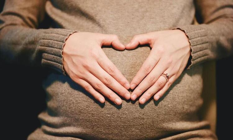 mulher grvida faz um corao com as mos sobre a barriga