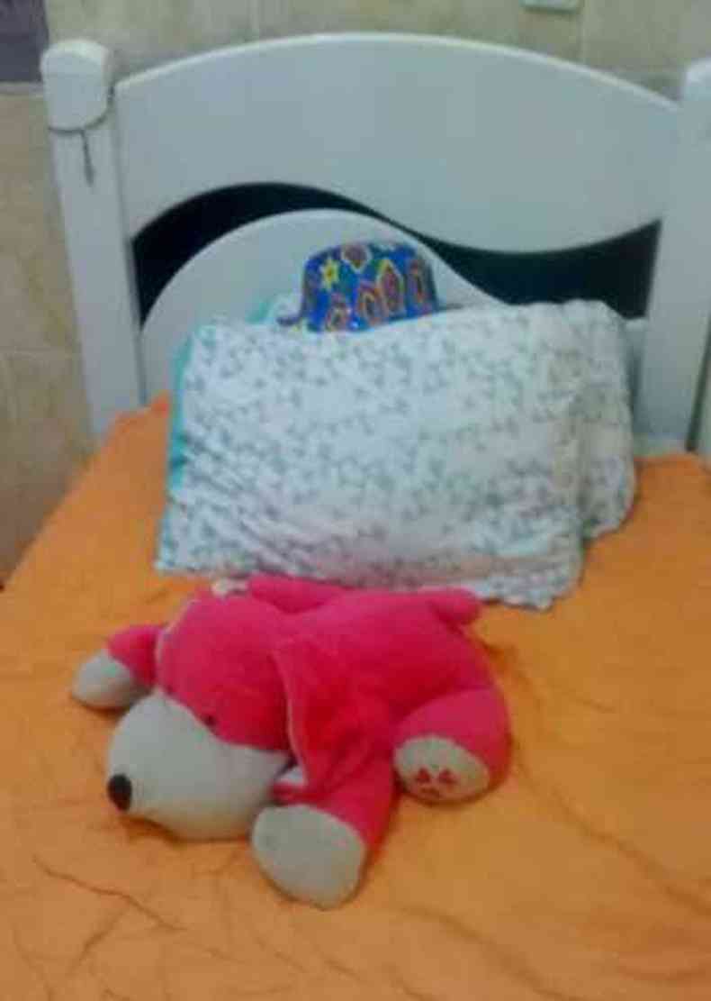 Cama com edredom laranja, urso rosa e travesseiros