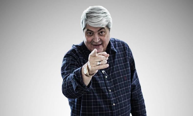 De p, Datena aponta o dedo para a foto enquanto sorri