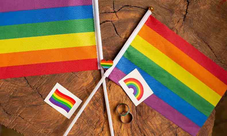 Duas bandeiras com as cores do arco-ris cruzadas sobre uma superfcie de madeira, junto com adesivos e anis tambm com a bandeira LGBT