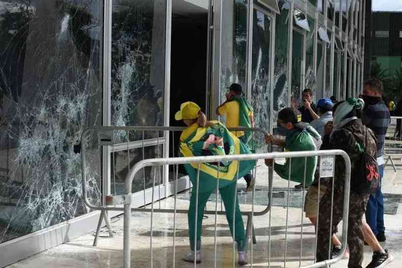 pessoas de verde e amarelo e enroladas em bandeiras do Brasil quebram vidros do Palcio do PLanalto