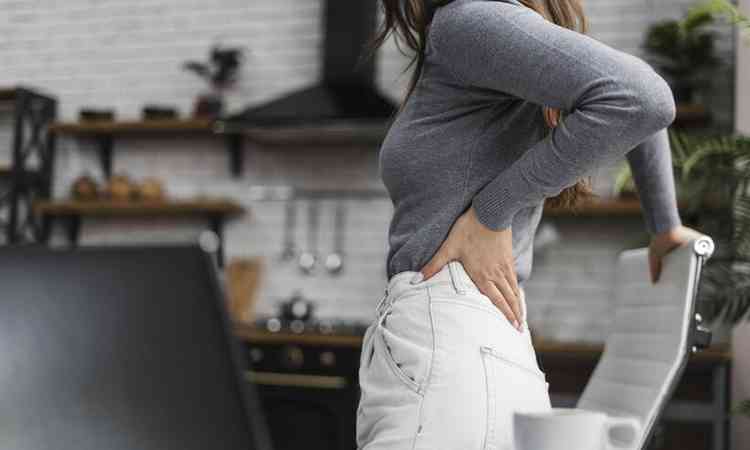 mulher com dor nas costas enquanto trabalha em casa