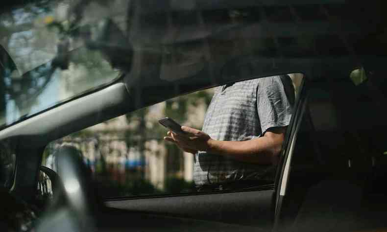 Pessoa usando o celular perto de um carro