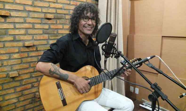 Cantor Luiz Caldas sorri, no estdio, sentado num banco e segurando o violo