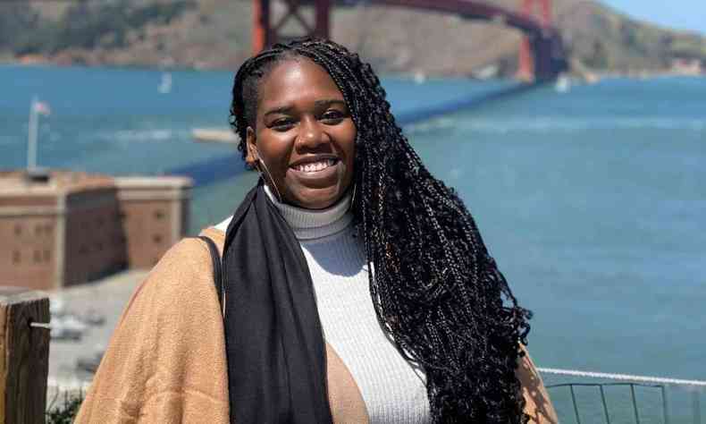 Danielle Marques, mulher preta com cabelos longos tranados, posando em frente  ponte Golden Gate