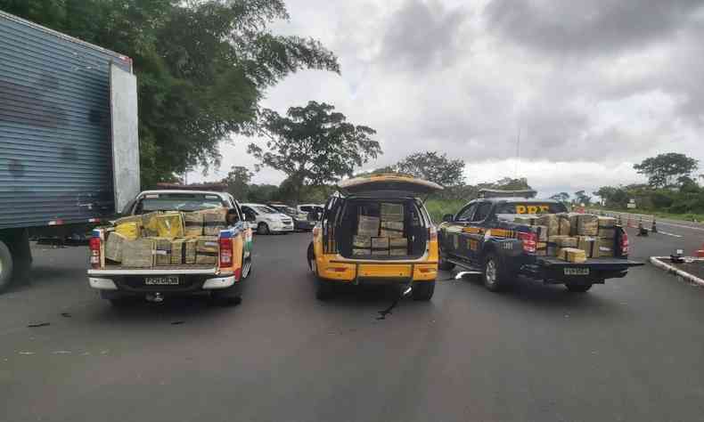 Trs viaturas policiais com parte da carga de maconha apreendida. No canto esquerdo aparece parte do compartimento de carga do caminho