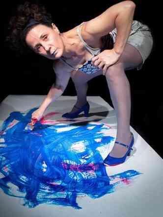 A atriz Rita Clemente olha para a cmera. Com as pernas inclinadas, ela tem pincel na mo direita e pinta o cho de azul