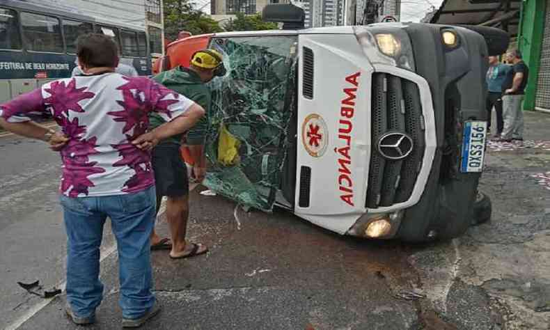 Ambulncia de lado, com vidros quebrados e pessoas em volta