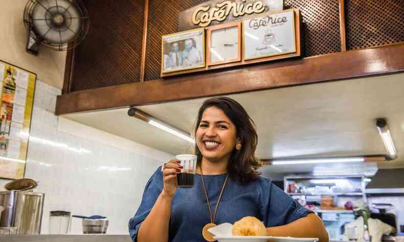 Mulher sorri para foto enquanto toma caf e come po de queijo no Caf Nice