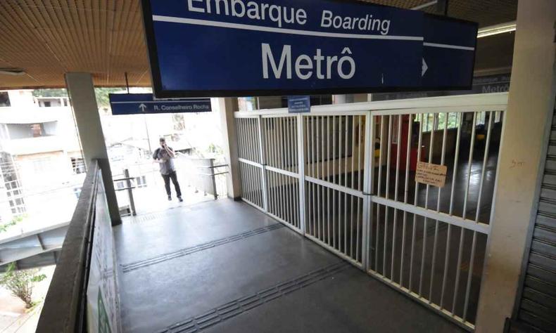 Parte interna da entrada do metr de Belo Horizonte. Um homem aparece ao fundo de um corredor que d acesso  uma rea externa. Em primeiro plano aparece uma placca pendurada no teto, de cor azul, escrito 'metr' na cor branca