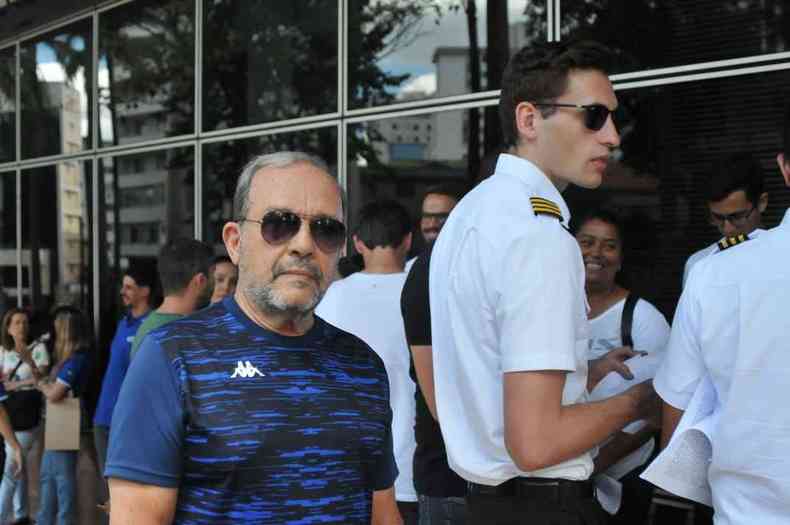 Homem em p vestindo uma camisa azul e culos escuros