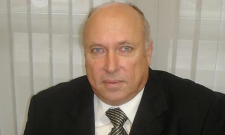 Jorge Borba  um homem branco de olhos azuis e cabelos grisalhos e ralos. Ele usa um terno preto com uma camisa social branca e gravata verde